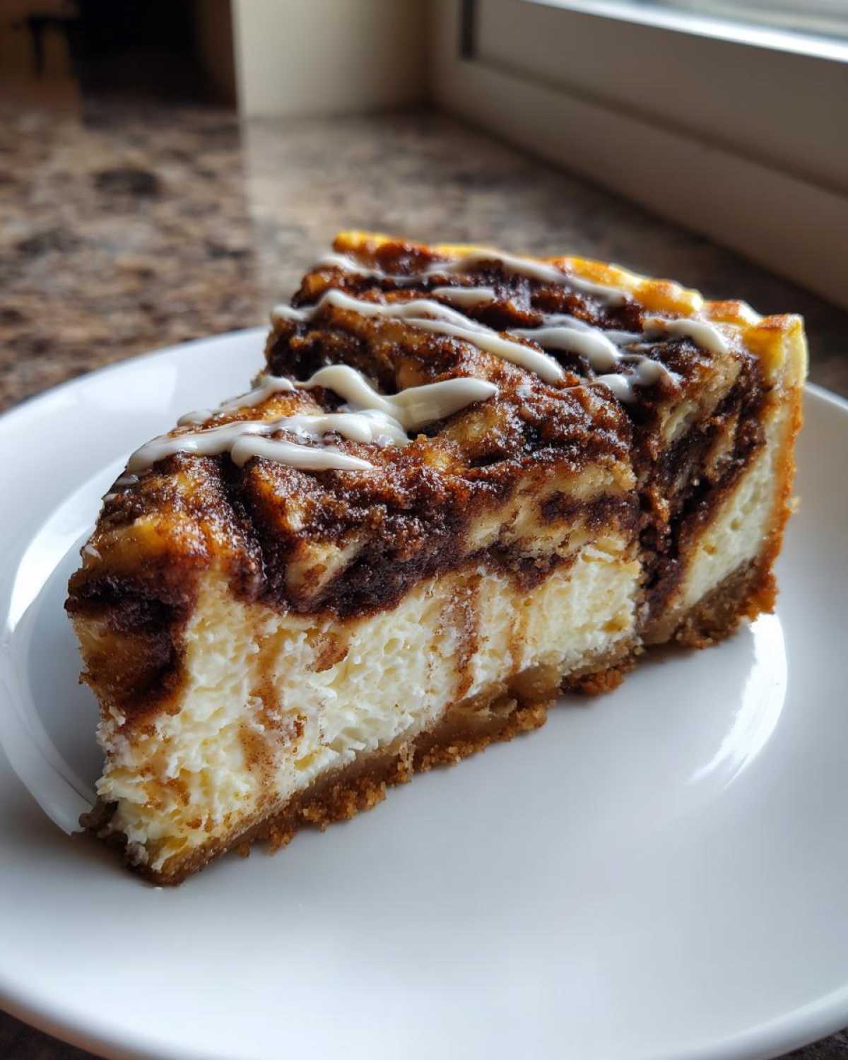 A close-up of a rich slice of Cinnamon Roll Cheesecake with a marbled cinnamon swirl and white icing drizzle.