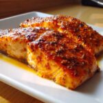 Two glistening fillets of Copycat Baked Salmon Texas Roadhouse with a thick, spiced glaze on a white plate.