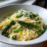Close-up of creamy Asparagus Orzo topped with Parmesan cheese, bright green asparagus spears, and lemon zest.