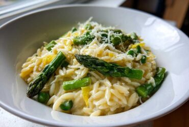 Close-up of creamy Asparagus Orzo topped with Parmesan cheese, bright green asparagus spears, and lemon zest.