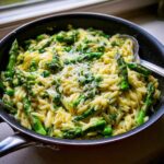 Close-up of creamy Asparagus Orzo mixed with bright green asparagus spears and peas, topped with grated Parmesan cheese.