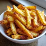 A close-up of golden brown, seasoned Crispy Air Fryer French Fries piled high in a small white bowl.