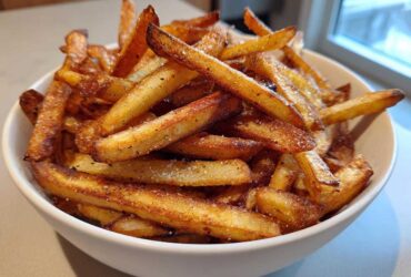 A close-up of a white bowl filled with golden brown, crispy air fryer french fries seasoned with salt and pepper.