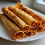 A stack of golden brown, crispy oven rolled chicken taquitos resting on a white plate.