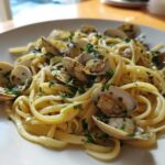 A close-up of a white plate filled with delicious Linguine and Clams tossed in a white wine sauce and fresh parsley.
