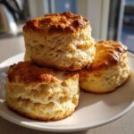Three tall, fluffy Cream Scones with golden brown tops stacked on a white plate, showing flaky layers.