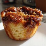 Close-up of a single, golden French Toast Muffin with a thick, sticky, caramelized pecan topping.