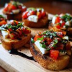 Close-up of several Fresh Caprese Crostini topped with tomato, mozzarella, basil, and balsamic glaze on a wooden board.