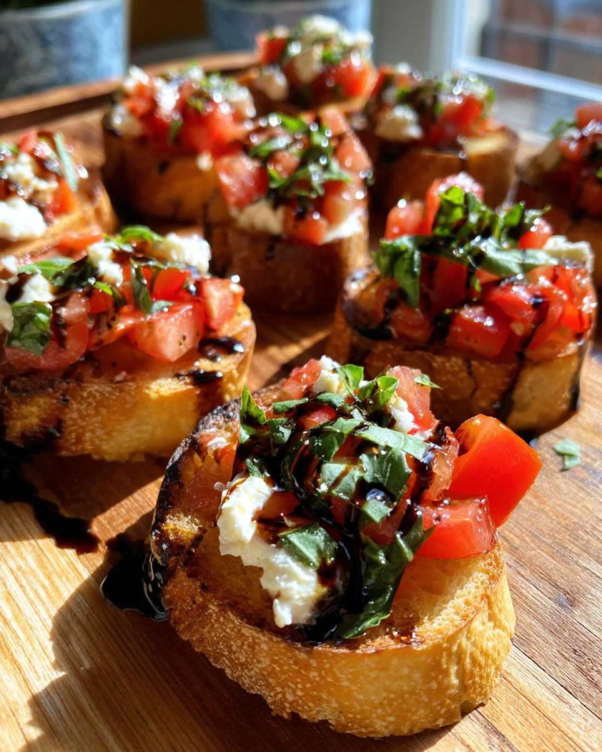 Several pieces of Fresh Caprese Crostini topped with mozzarella, tomatoes, basil, and balsamic glaze, arranged on a wooden serving board.