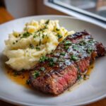 A perfectly cooked Garlic Butter Steak, sliced to show medium-rare interior, served next to creamy mash potatoes, drizzled with garlic butter sauce.