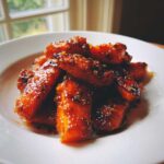 Close-up of Glazed Honey Garlic Butter Roasted Carrots piled on a white plate, shining with glaze.