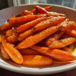 Close-up of bright orange Glazed Honey Garlic Butter Roasted Carrots piled high in a white serving bowl.
