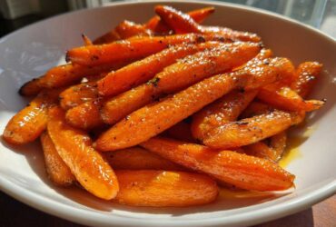 Close-up of bright orange Glazed Honey Garlic Butter Roasted Carrots piled high in a white serving bowl.