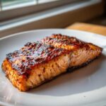 A perfectly cooked, glazed salmon fillet resting on a white plate, showcasing the rich color from the Salmon Marinade for Grilled Dinner.