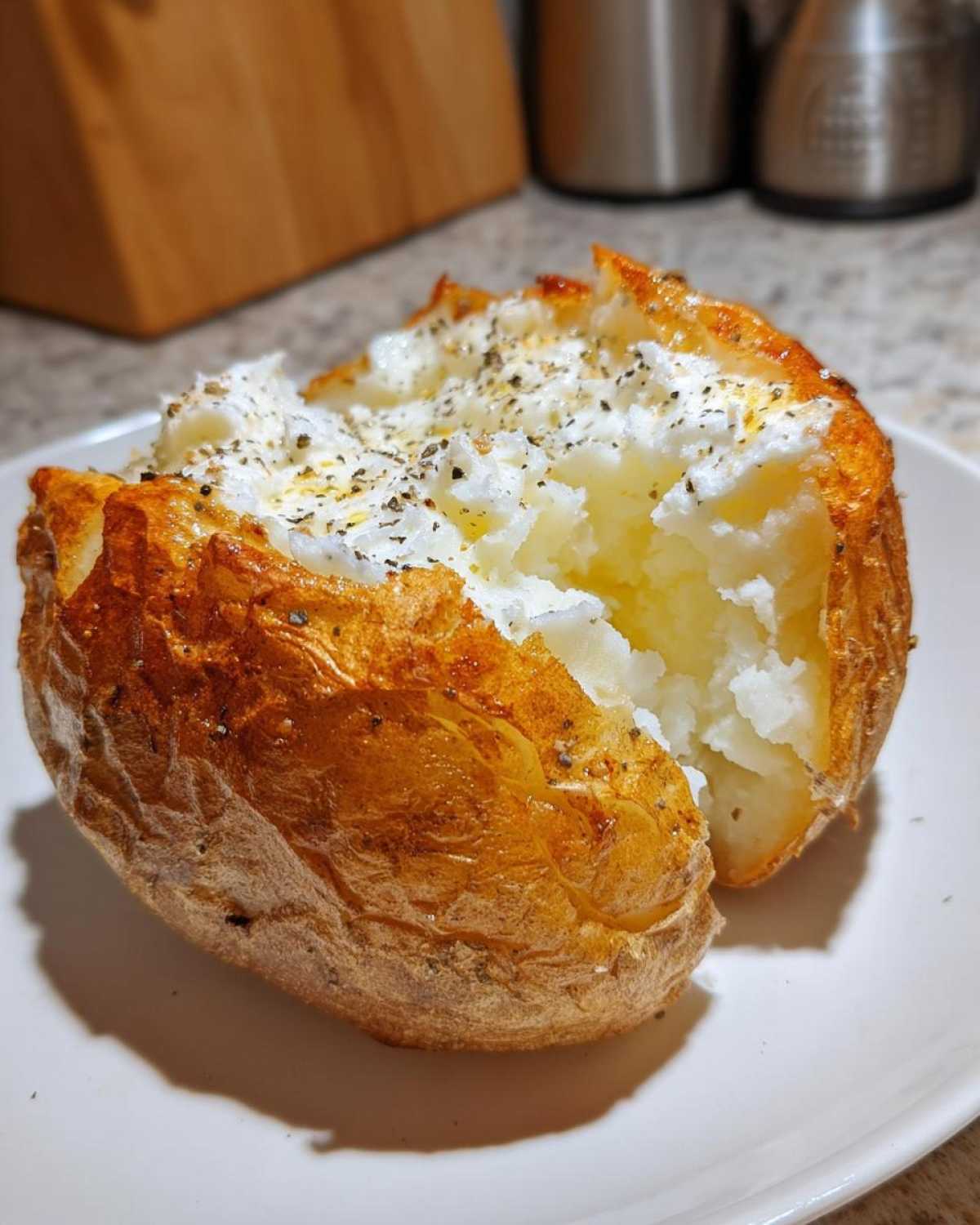 A perfectly cooked Gordon Ramsay Baked Potatoes, split open to show fluffy interior topped with butter and herbs.