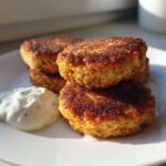 A stack of three golden brown, pan-fried Irresistible Salmon Patties served with a dollop of creamy white dipping sauce.