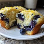 Close-up of a moist Lemon Blueberry Muffins cut in half, revealing juicy blueberries and lemon zest topping.