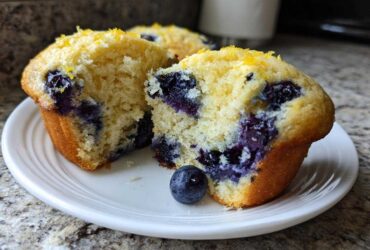 Close-up of a moist Lemon Blueberry Muffins cut in half, revealing juicy blueberries and lemon zest topping.