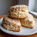 Three fluffy Lemon Vanilla Scones stacked on a plate, drizzled with thick white lemon glaze and zest.