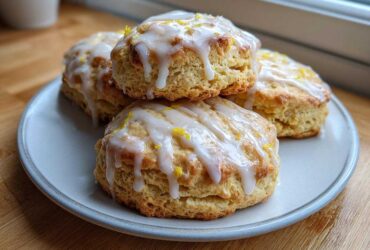 A stack of four freshly baked Lemon Vanilla Scones topped with white glaze and bright yellow lemon zest.