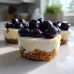 Close-up of a single mini cheesecake topped with glossy blueberry compote, one of several Little Blueberry Cheesecakes Sweet Treats.
