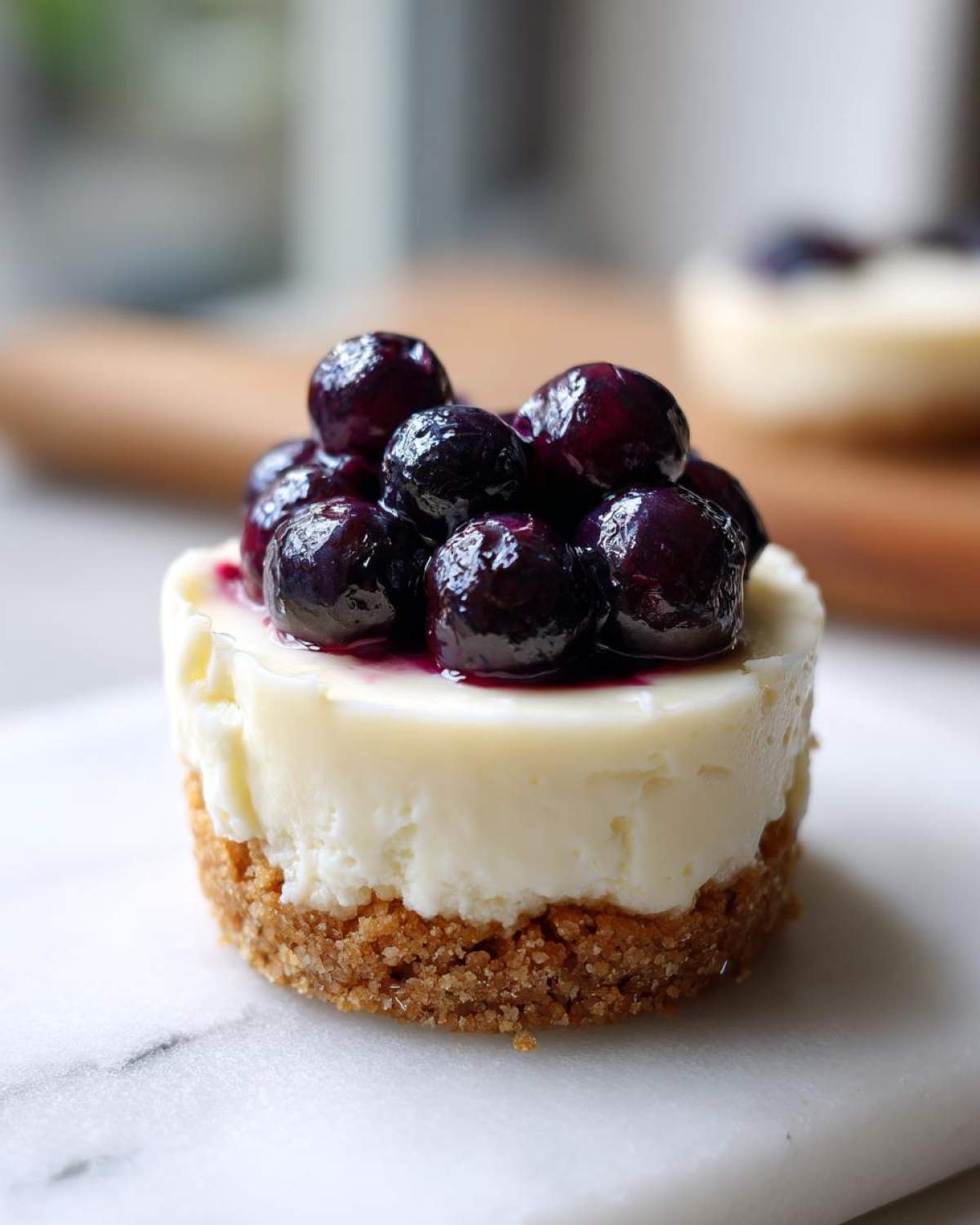 A close-up of one of the Little Blueberry Cheesecakes Sweet Treats, featuring a graham cracker crust and creamy filling topped with fresh blueberries.