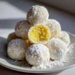 A stack of No Bake Lemon Truffles coated in powdered sugar, with one cut open revealing the bright yellow interior.