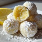 A pile of No Bake Lemon Truffles dusted heavily with powdered sugar next to a lemon half.