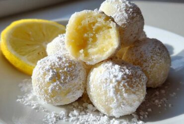 A pile of No Bake Lemon Truffles dusted heavily with powdered sugar next to a lemon half.