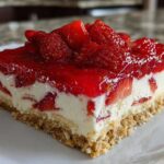 Close-up of a square slice of No Bake Strawberry Lasagna showing a graham cracker crust, creamy filling, and bright red strawberry glaze topping.