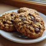 Three freshly baked oatmeal chocolate chip Go Bananas Cookies stacked on a small white plate.