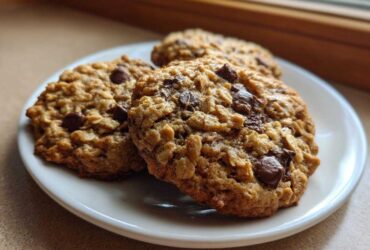Three freshly baked oatmeal chocolate chip Go Bananas Cookies stacked on a small white plate.