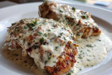 Two golden-brown chicken breasts smothered in creamy Parmesan chicken with garlic sauce and sprinkled with fresh parsley.