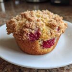A single, perfect Raspberry Streusel Muffins on a white plate, featuring a golden crumb topping and visible fresh raspberries.