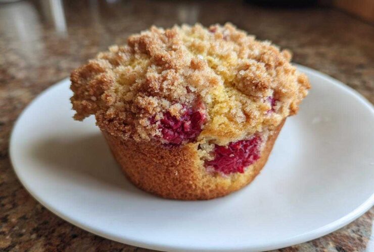 A single, perfect Raspberry Streusel Muffins on a white plate, featuring a golden crumb topping and visible fresh raspberries.