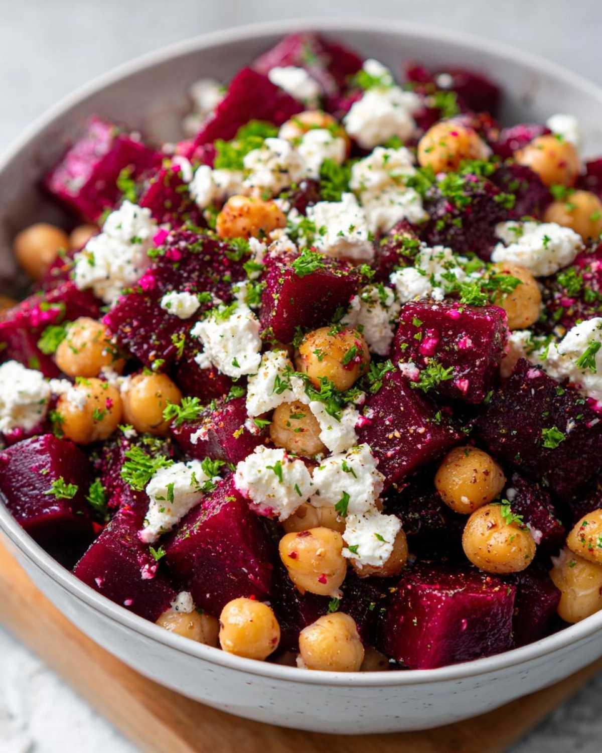 Close-up of a bowl filled with cubes of deep red beets, chickpeas, and crumbled white feta cheese, garnished with parsley for a Refreshing Chickpea Beet Feta Salad.