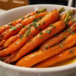 Close-up of shiny, glazed Roasted Carrots Hot Honey Butter garnished with fresh parsley in a white serving bowl.
