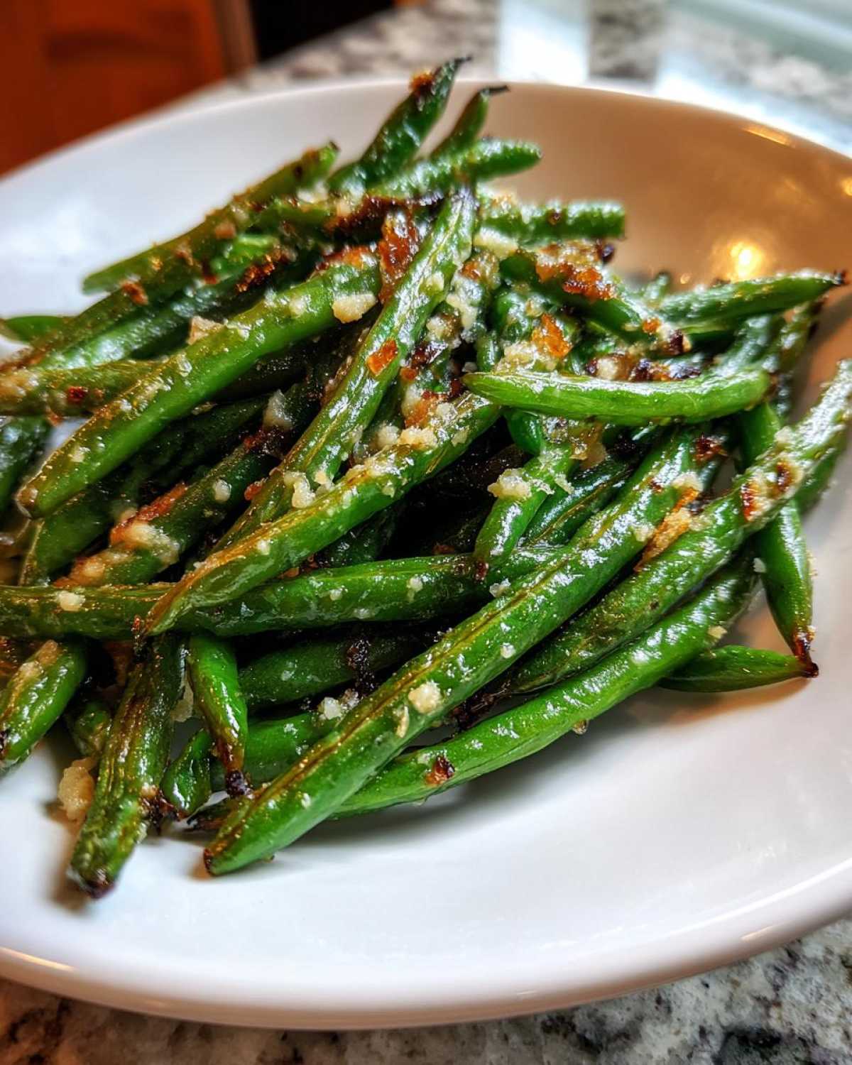 A bowl filled with vibrant green Roasted Garlic Parmesan Green Beans, topped with visible minced garlic and browned Parmesan cheese.