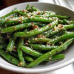 Close-up of bright green Roasted Garlic Parmesan Green Beans topped with crispy garlic and cheese in a white bowl.