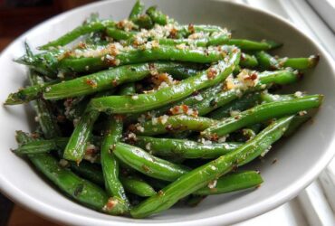 Close-up of bright green Roasted Garlic Parmesan Green Beans topped with crispy garlic and cheese in a white bowl.