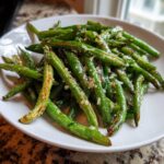Close-up of bright green Roasted Garlic Parmesan Green Beans tossed with minced garlic and cheese on a white plate.