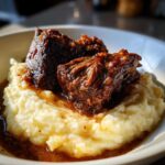Two tender, glazed Slow Cooker Beef Short Ribs served atop a generous portion of creamy mashed potatoes.