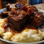 Close-up of tender Slow Cooker Beef Short Ribs smothered in rich gravy served over creamy mashed potatoes in a bowl.