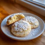 Three Soft & Chewy Lemon Sugar Cookies dusted heavily with powdered sugar on a white plate.