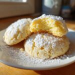 Three Soft & Chewy Lemon Sugar Cookies dusted heavily with powdered sugar on a white plate.