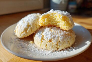 Three Soft & Chewy Lemon Sugar Cookies dusted heavily with powdered sugar on a white plate.