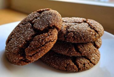 A close-up stack of four dark brown, crinkled Soft & Chewy Molasses Cookies generously coated in sparkling granulated sugar.