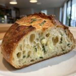 Close-up of a Sourdough Artisan Loaf Recipe with Italian Herbs and Cheese cut in half, showing open crumb and melted cheese pockets.