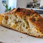 Close-up of a slice showing the open crumb structure of the Sourdough Artisan Loaf Recipe With Italian Herbs and Cheese.