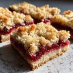 A close-up of a delicious Strawberry Shortcake Bars square showing the buttery crust, thick strawberry filling, and crumb topping.